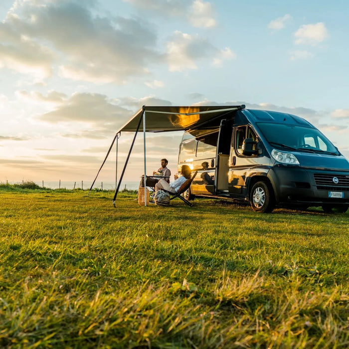Fiamma wind-out awning extended on a campervan at sunset with people relaxing in camping chairs
