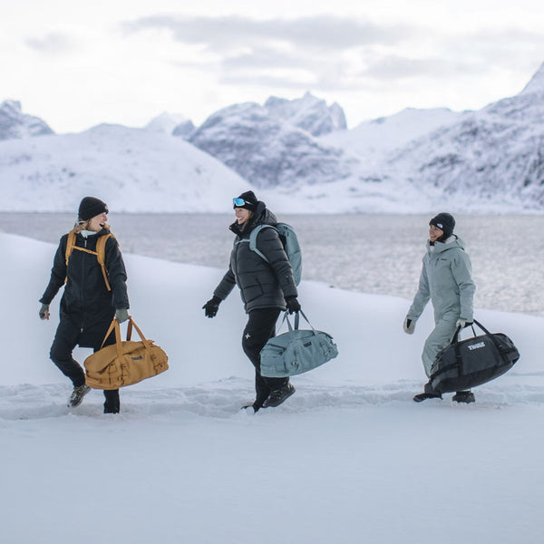 Three people walking in snow carrying Thule camping bags and rucksacks
