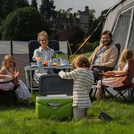 Family of five eating at a camping table with food in sunshine