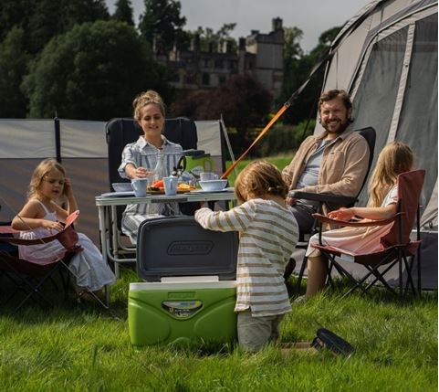 Family of five eating at a camping table with food in sunshine