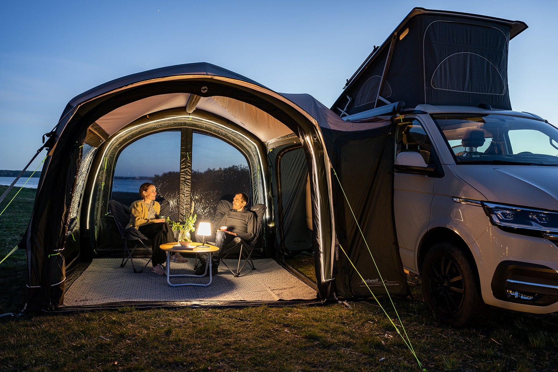 Drive-away awning lit up in the evening with people relaxing in camp chairs