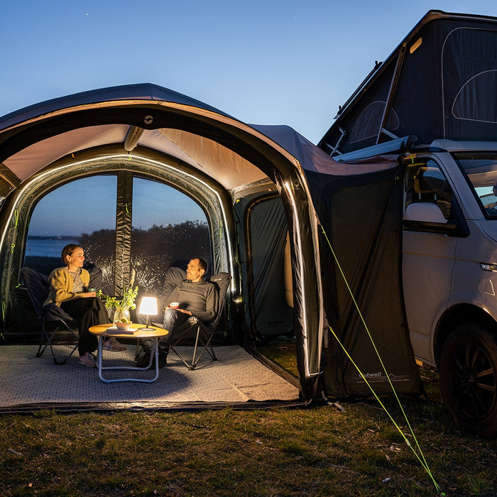 Drive-away awning lit up in the evening with people relaxing in camp chairs