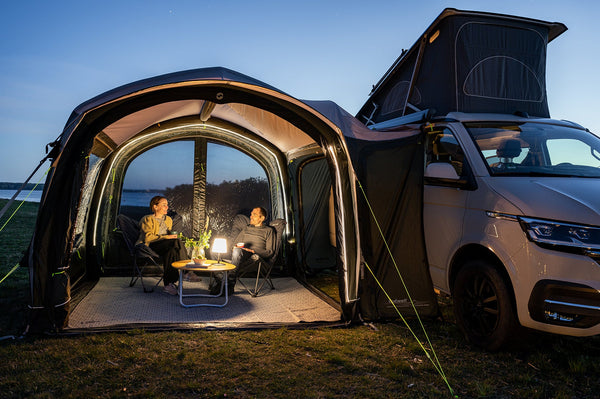 Drive-away awning lit up in the evening with people relaxing in camp chairs