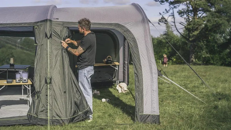Outwell air tent being set up with side panel tied back and children playing nearby in a grassy field
