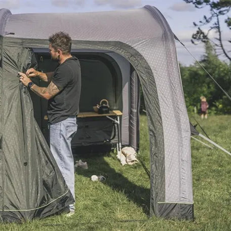 Outwell air tent being set up with side panel tied back and children playing nearby in a grassy field