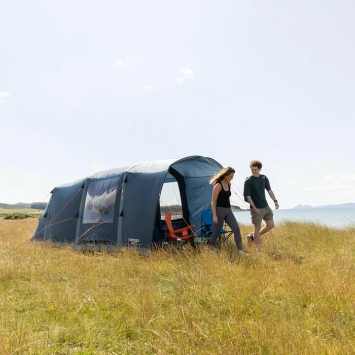Vango 2 person tent pitched in a grassy field with a man admiring the view in sunshine