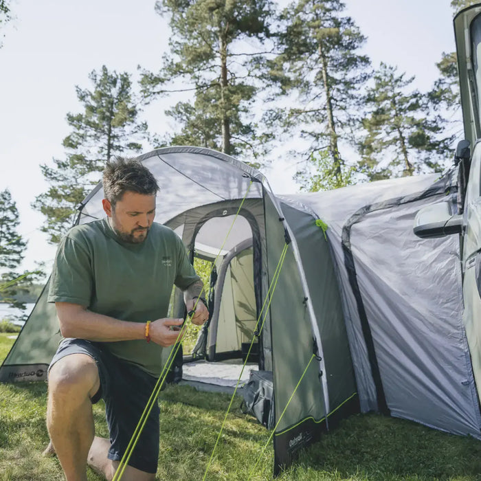 Outwell Talladega Air drive-away awning being pitched with a person pegging a guyline in sunshine