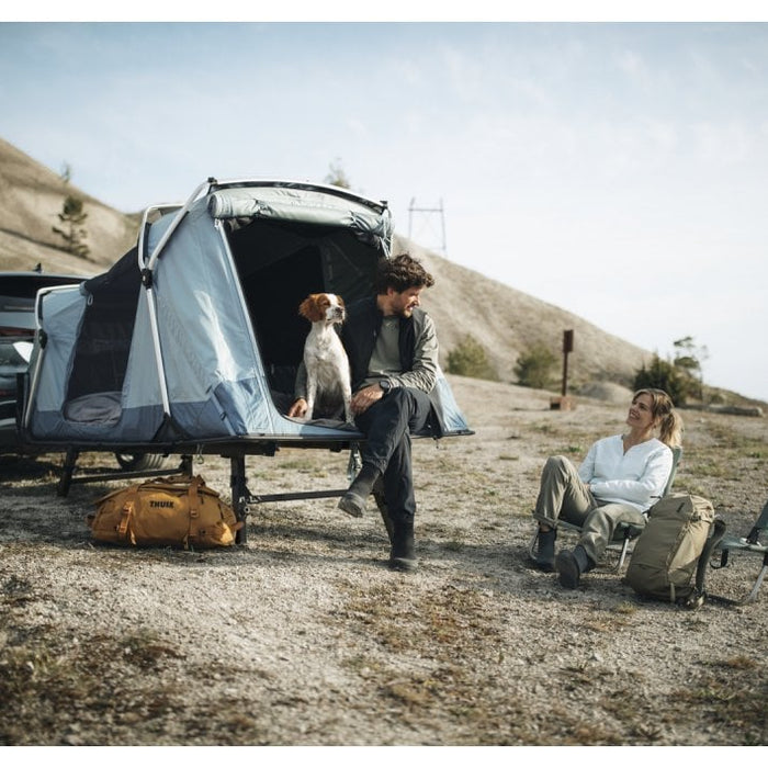 Thule Outset tailgate tent with camping setup, two adults and a dog smiling beside their vehicle