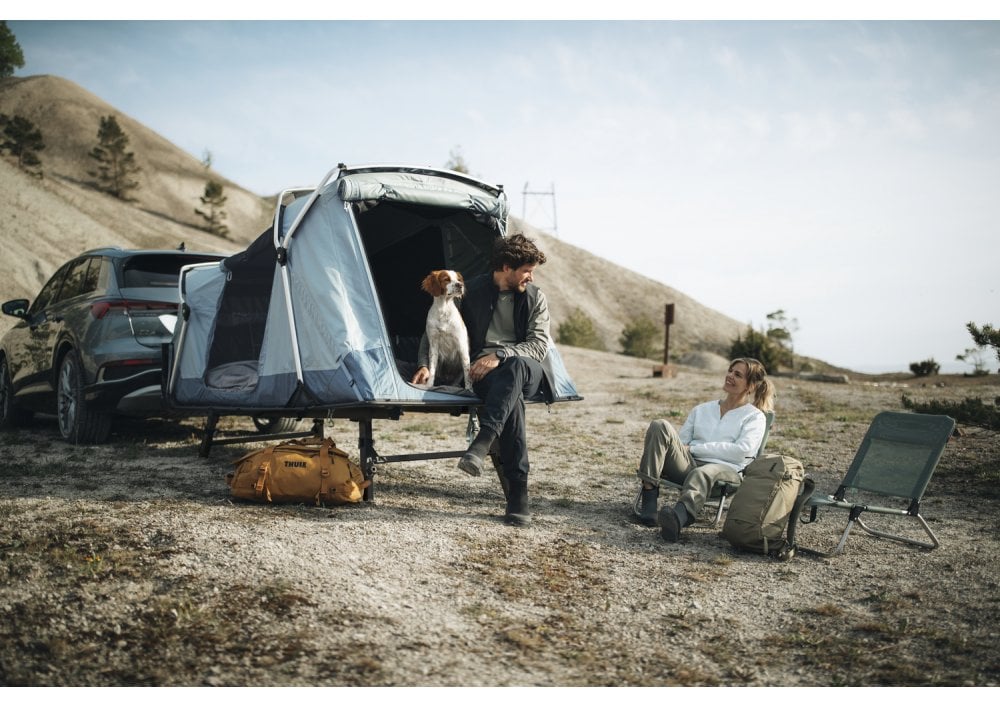 Thule Outset tailgate tent with camping setup, two adults and a dog smiling beside their vehicle