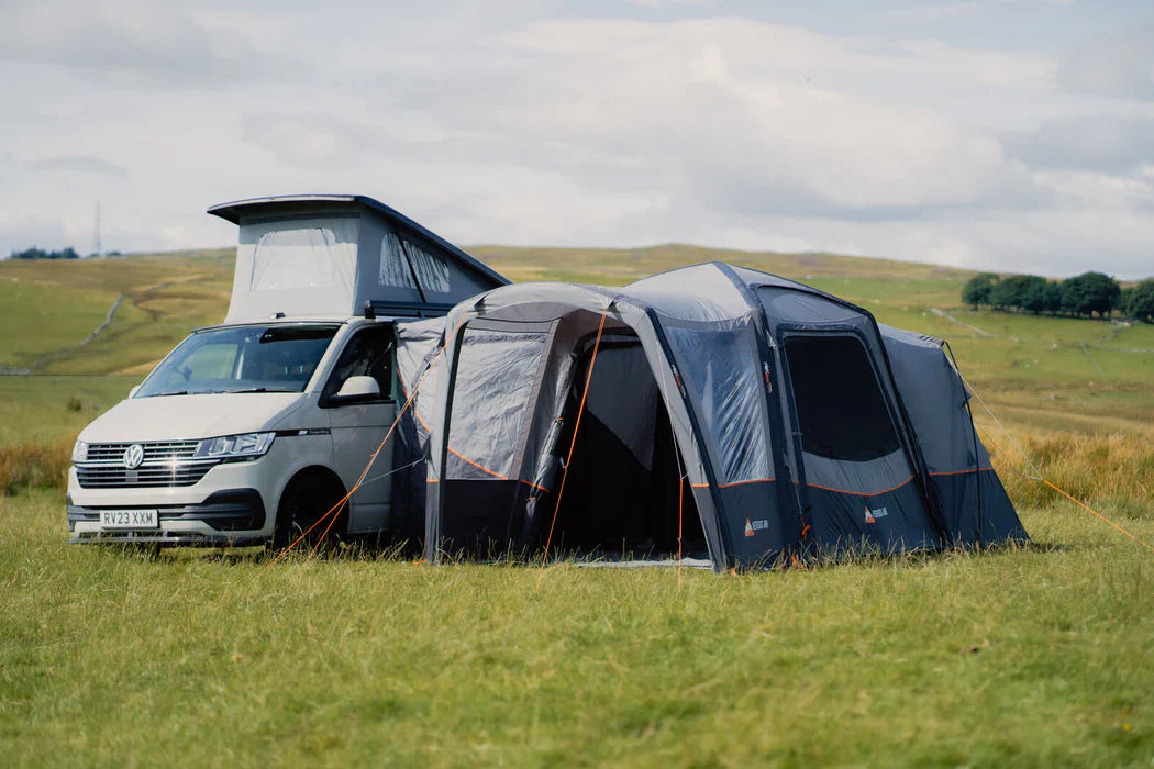 Vango Versos Air inflatable drive-away awning attached to a campervan with a camping table in a grassy field in sunshine