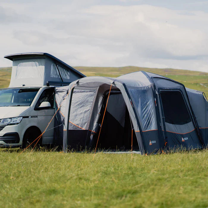 Vango Versos Air inflatable drive-away awning attached to a campervan with a camping table in a grassy field in sunshine
