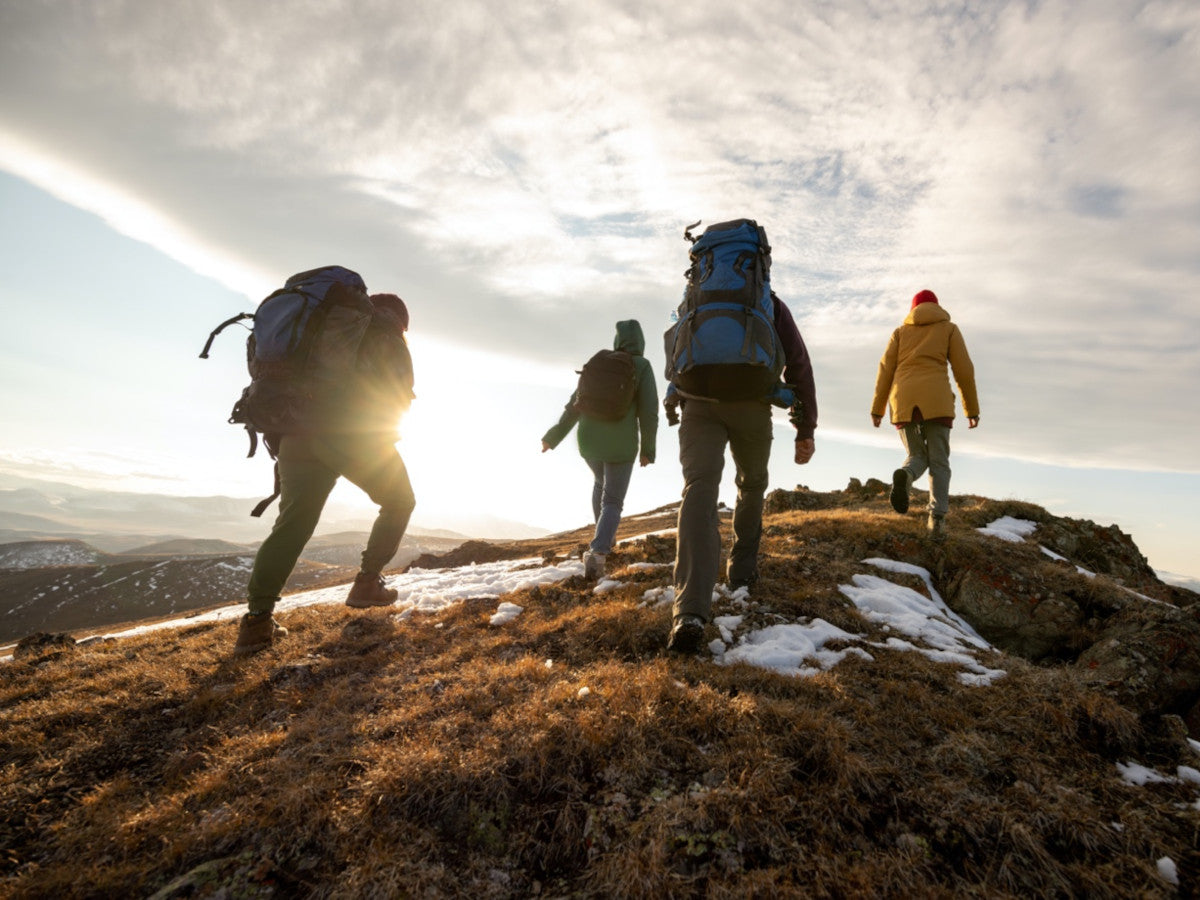 four people hiking with backpacks up a mountain into the sunrise 